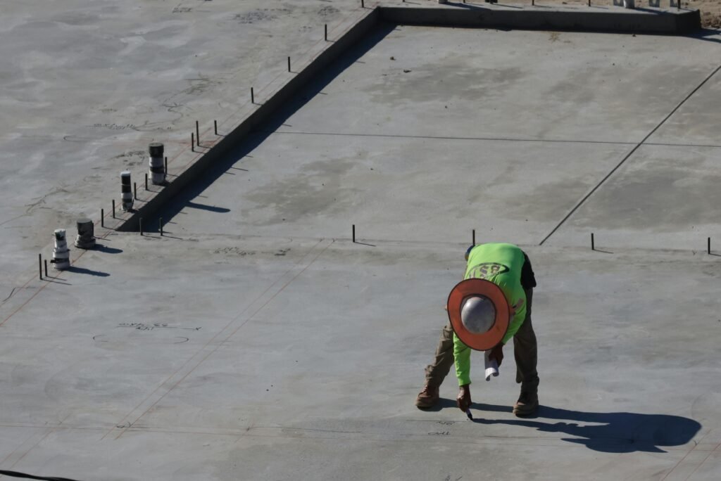 Construction worker in bright sun, bending on urban site with concrete slab.